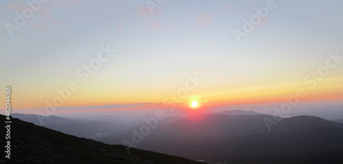 Colorful sun setting over peaks looking out from the Appalachian Trail on Mt. Washington, White Mountains, New Hampshire, mountains in silhouette. Suitable for background, with copy space.