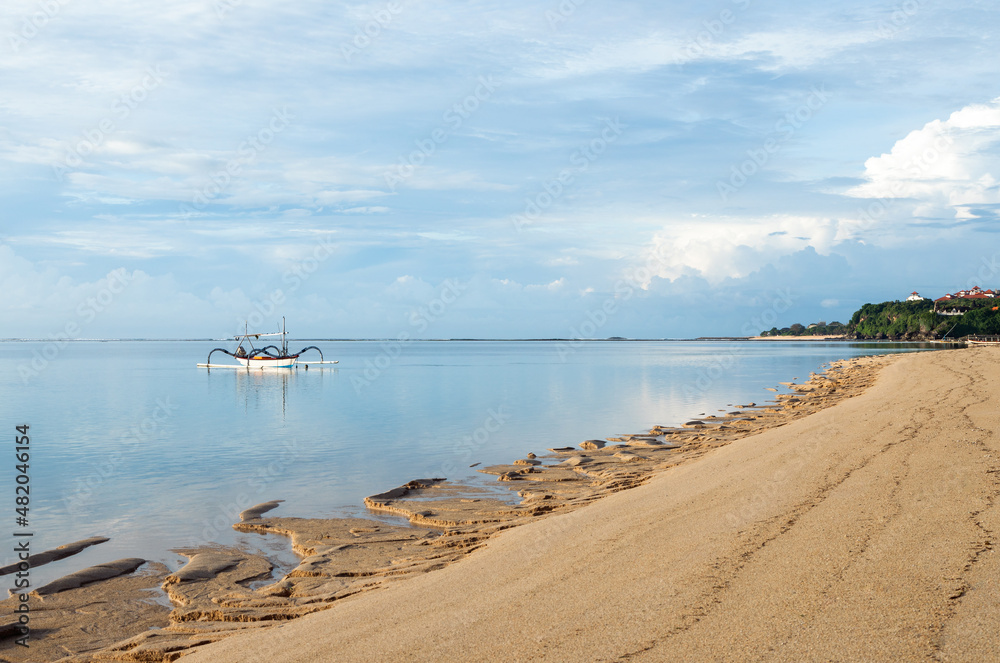 Nusa dua beach, Bali island, Indonesia. Beautiful summertime view ocean on the white sand beach. Traditional fishing boats. BLue sky with clouds.