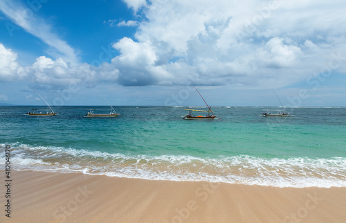 Fishing boats floating on the ocean. Wooden boat sailing in open waters. Sailing boat landscape. High waves with foam spread on the coast. Tropical landscape. Bali island, Indonesia. Summer vacation.