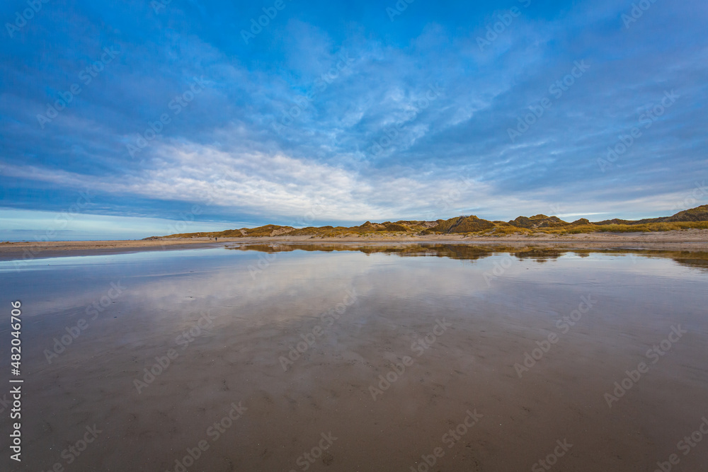 The blue and white winter sky above the beach and dunes of Amrum island, northern Germany, reflected by the smooth water surface