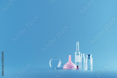 The small magnifying glass, pink funnel, ampoule, glass bottles on a blue background. The concept of research children's works, young chemists, a template for an announcement, a scientific conferences