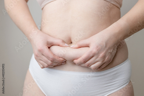 Fat woman hand holding fat belly on white background. Fat female belly, woman holding skin to check cellulite.