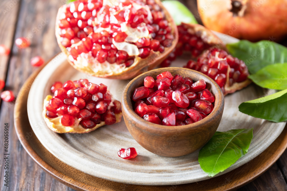 Ripe juicy pomegranate fruits in a wooden bowl on a rustic table closeup. Diet and healthy food. Ripe juicy pomegranate fruits in a wooden bowl on a rustic table closeup. Diet and healthy food.