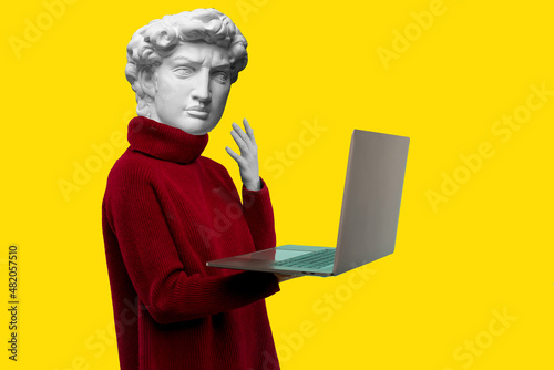 Abstract modern collage. The man with the plaster head of David in a red sweater looks at a laptop screen on a yellow background photo