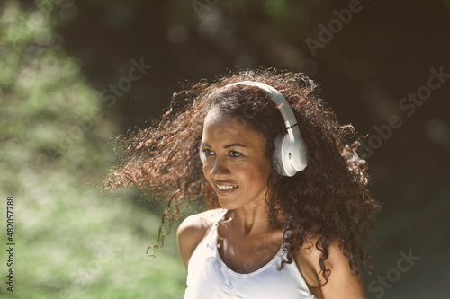 Excited girl dancing and listening music with headphones and smart phone in the park with hair moving