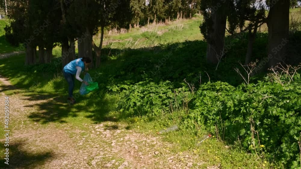 a female volunteer with a plastic bag of garbage walks along the road near the forest and collects garbage in a bag. n the frame of the volunteer's legs with a plastic bag. Video UHD slow motion