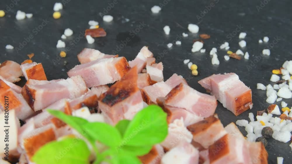 Dice bacon, basil and seasonings on rotating slate tray. Sliced bacon cubes, basil and seasonings on a rotating slate plate. Macro