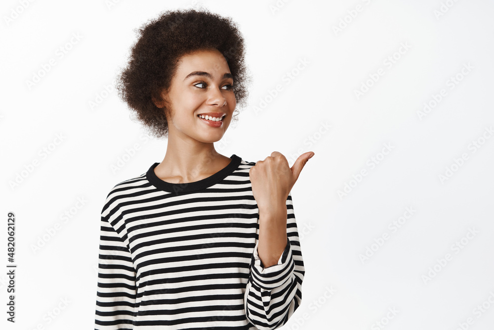 Portrait of smiling african girl pointing and looking right with pleased smile on face, showing logo, company brand banner, standing over white background Portrait of smiling african girl pointing and looking right with pleased smile on face, showing logo, company brand banner, standing over white background