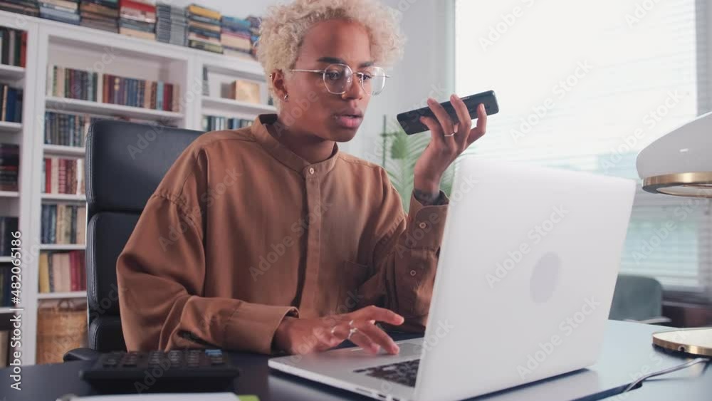 Young successful ethnic African American woman entrepreneur talking on mobile phone and typing on laptop working in multitasking mode sits on chair at table in own office. Professionalism, technology Young successful ethnic African American woman entrepreneur talking on mobile phone and typing on laptop working in multitasking mode sits on chair at table in own office. Professionalism, technology