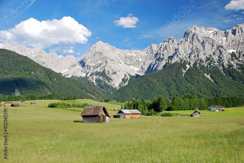 Huts on a green meadow surrounded by forest an the barren peaks of the bavarian alps