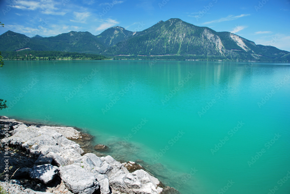 The smooth turquoise water of Lake Walchensee in the bavarian alps with mountains in the background and a white stone in the front
