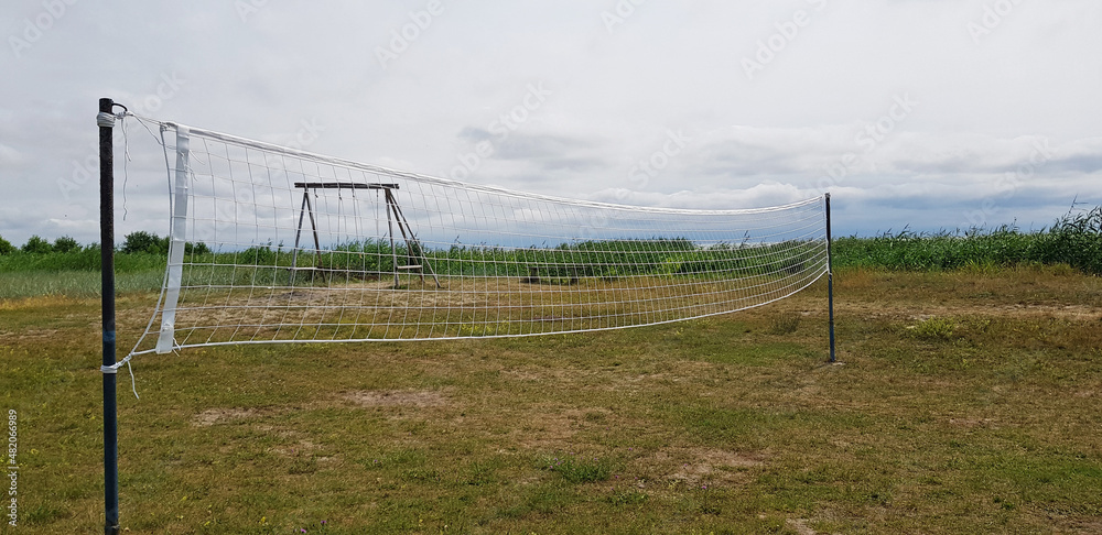volleyball net in the field in summer against the background of grass, blue sky and swings