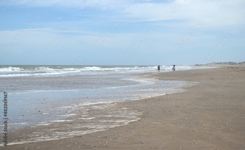 Pareja caminando a lo lejos en la playa un día nublado