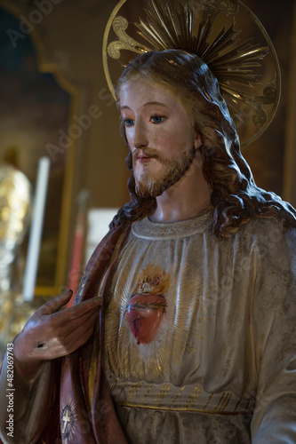 Ancient statue of Jesus Christ the Good Shepherd with hole in his hand pointing at his sacred heart and aureole - Biblical tradition, religion, Christianity, God, faith concept