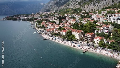 Smooth aerial of beautiful Kotor Old Town and marina bay shot with drone on summer day in Montenegro, view of historical architecture, tourist attractions, boats in harbor, people on beach park