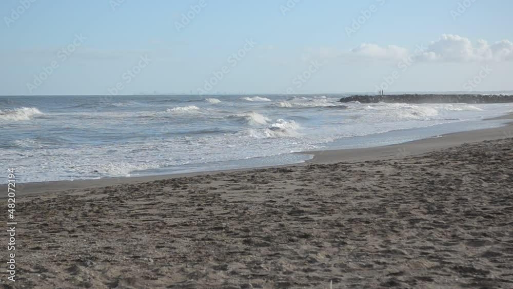 Las olas y el viento en una playa solitaria con unos pocos pescadores a lo lejos