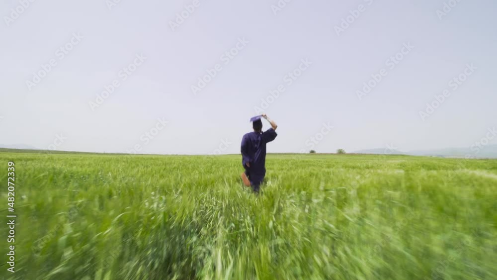 Young man with graduation clothes running in a green field throwing hat in the air.. Young man with graduation clothes running in a green field throwing hat in the air..