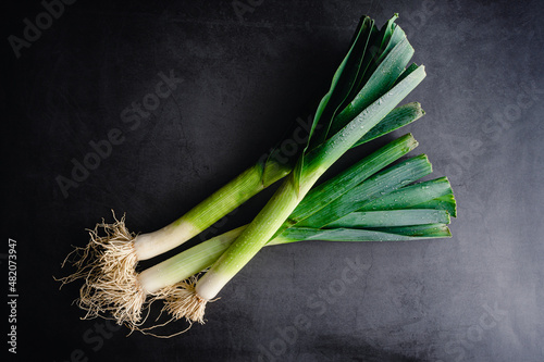 Overhead View of Whole Leeks on a Dark Background: Three leeks with leaves and roots on a stone countertop photo