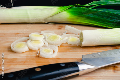 Sliced Leeks on a Bamboo Cutting Board: Sliced and whole leeks with a chef's knife on a wooden cutting board