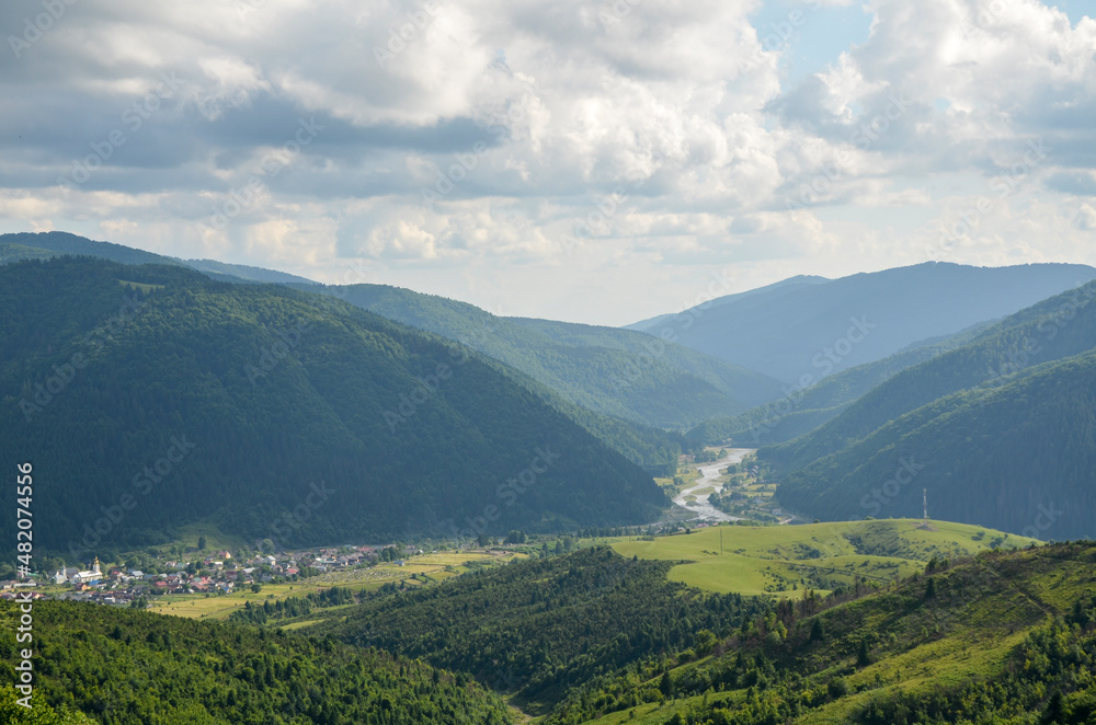 River flowing through mountain valley covered with dense forests under cloudy sky. Carpathian mountains, Ukraine River flowing through mountain valley covered with dense forests under cloudy sky. Carpathian mountains, Ukraine