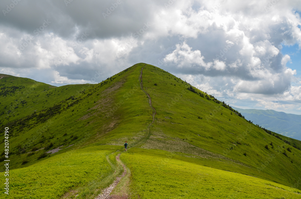 Tourist trail passes over the green grassy peak of mountain ridge. Trekking in Carpathian Mountains, Ukraine
Tourist trail passes over the green grassy peak of mountain ridge. Trekking in Carpathian Mountains, Ukraine
