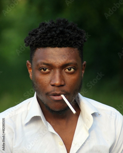 Portrait of a young African-American man in a white shirt with a cigarette.