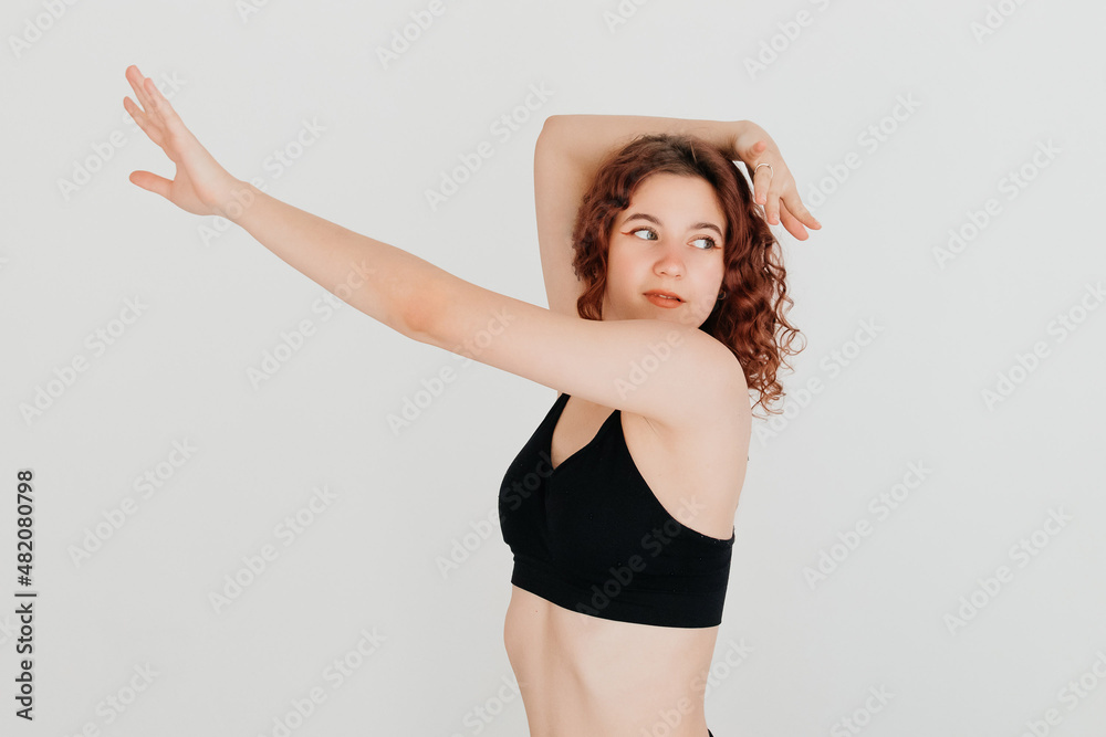 Positive redhead woman dancer training in the studio, looking to the side, stretching her arm. Active young woman in casual summer outfit having fun indoor Positive redhead woman dancer training in the studio, looking to the side, stretching her arm. Active young woman in casual summer outfit having fun indoor