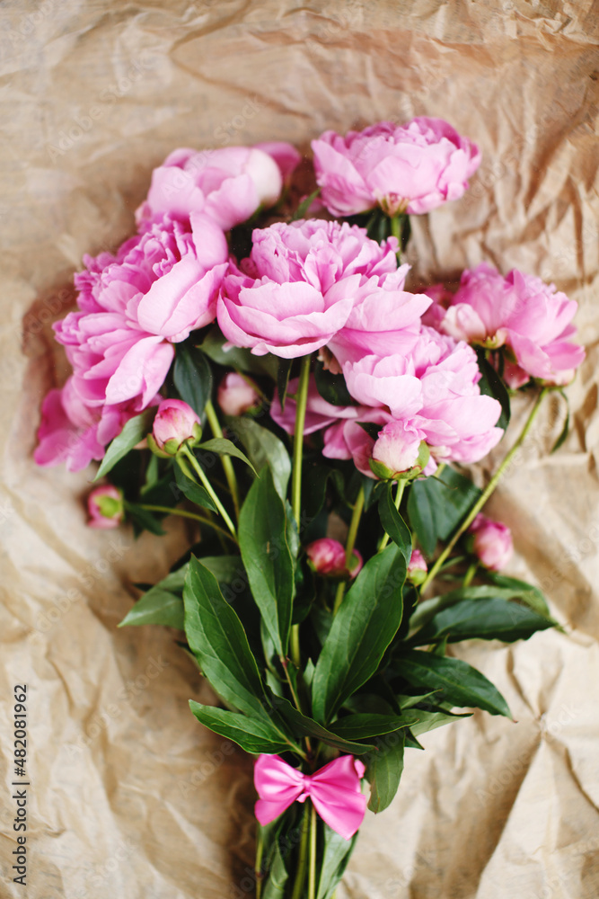 Tender bouquet of pink peonies flowers in sunlight on wrinkled craft paper background