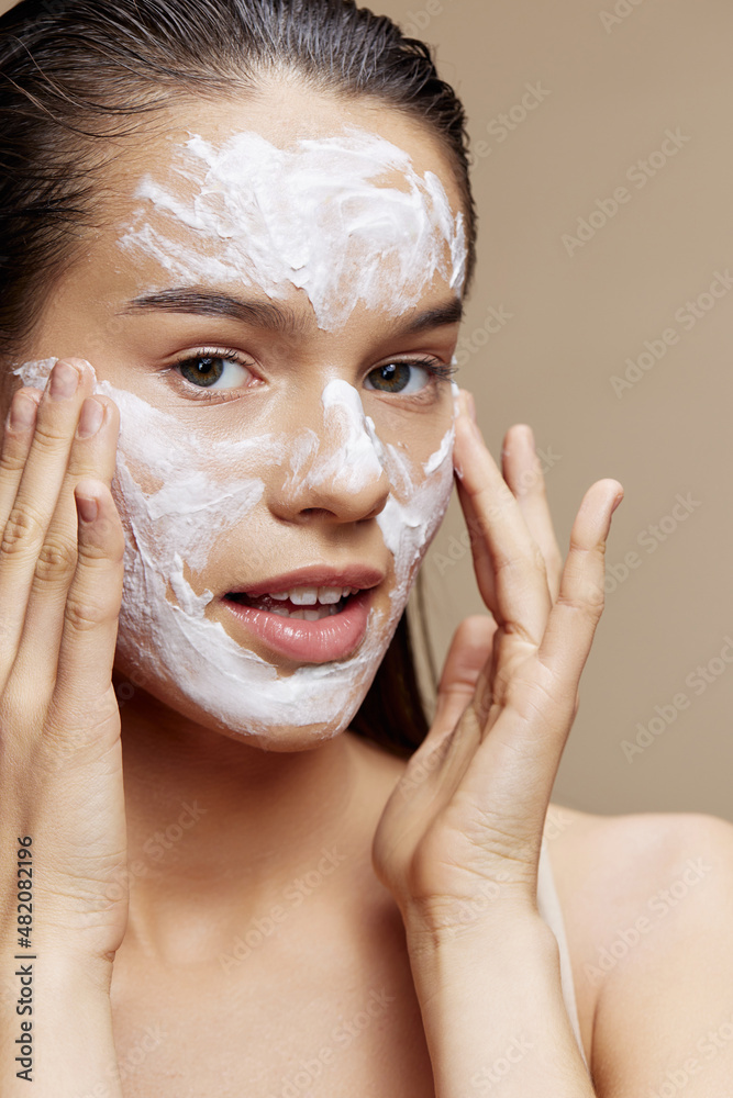 young woman face mask cream clean skin facial scrub beige background