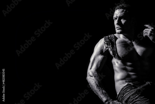 Strong brutal guy. Sexy torso. Leather belt, jeans. Handsome big muscles man posing at studio. Model showing torso with six pack abs. Isolated on black background. Showing muscular torso