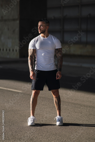chico con tatuajes haciendo deporte en la calle con una camiseta blanca y pantalones cortos photo