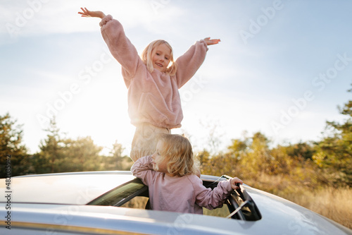 Sisters standing in sunroof of car photo