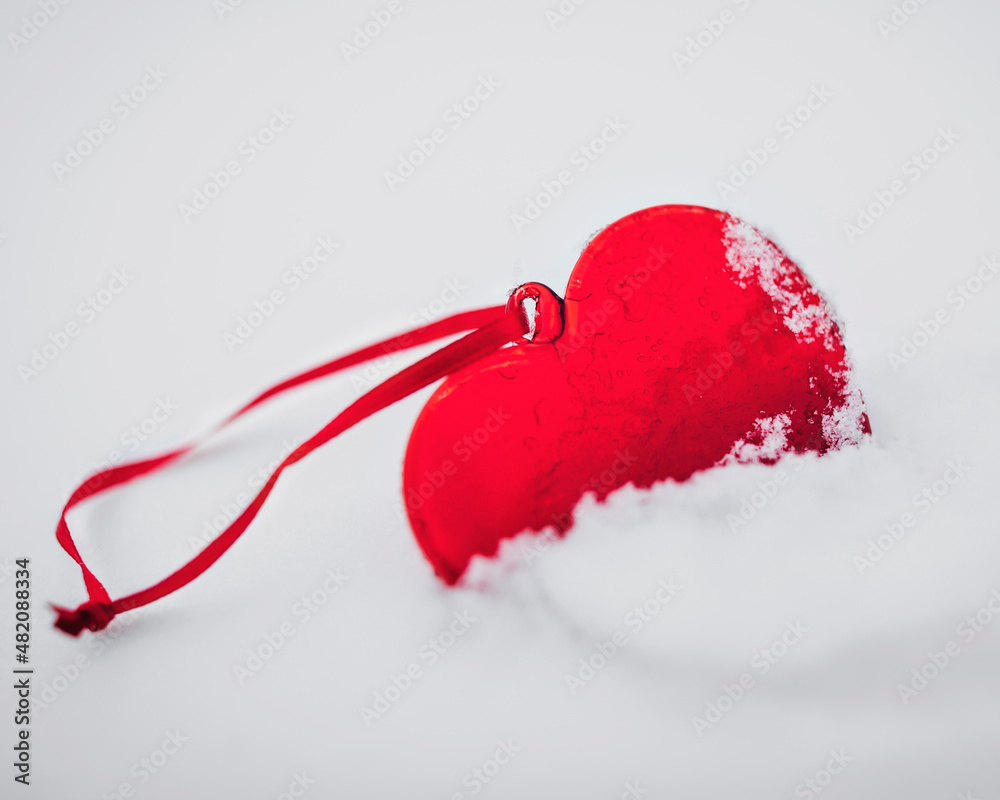 Beautiful glassy red heart in the snow. In a snow winter background. The 14th of February. Saint Valentine's Day.  Love and St. Valentine day concept. Frozen heart. Red on white