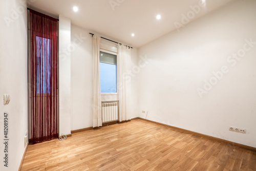 Empty room with light oak wooden floor, aluminum radiators and red and white curtains