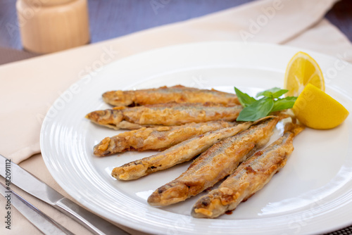 fried smelt on a white plate with lemon side view