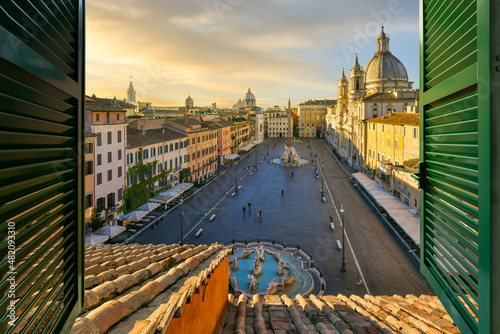 Beautiful sunset view from a penthouse resort hotel room through a window with shutters of the famous Piazza Navona in Rome, Italy.