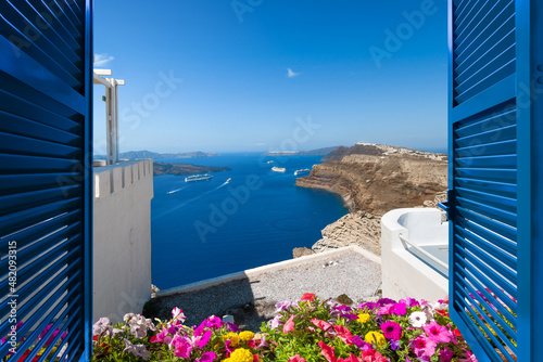 View from a terrace room with shutters and flowers of the Aegean Sea and caldera in the village of Oia on the island of Santorini, Greece. 