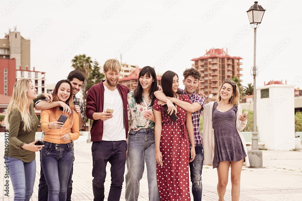Multicultural row of friends walking together holding mobile smart phone  outdoors. Interracial happy couples having fun day at city centre.  Friendship and modern technology concept. Stock Photo | Adobe Stock