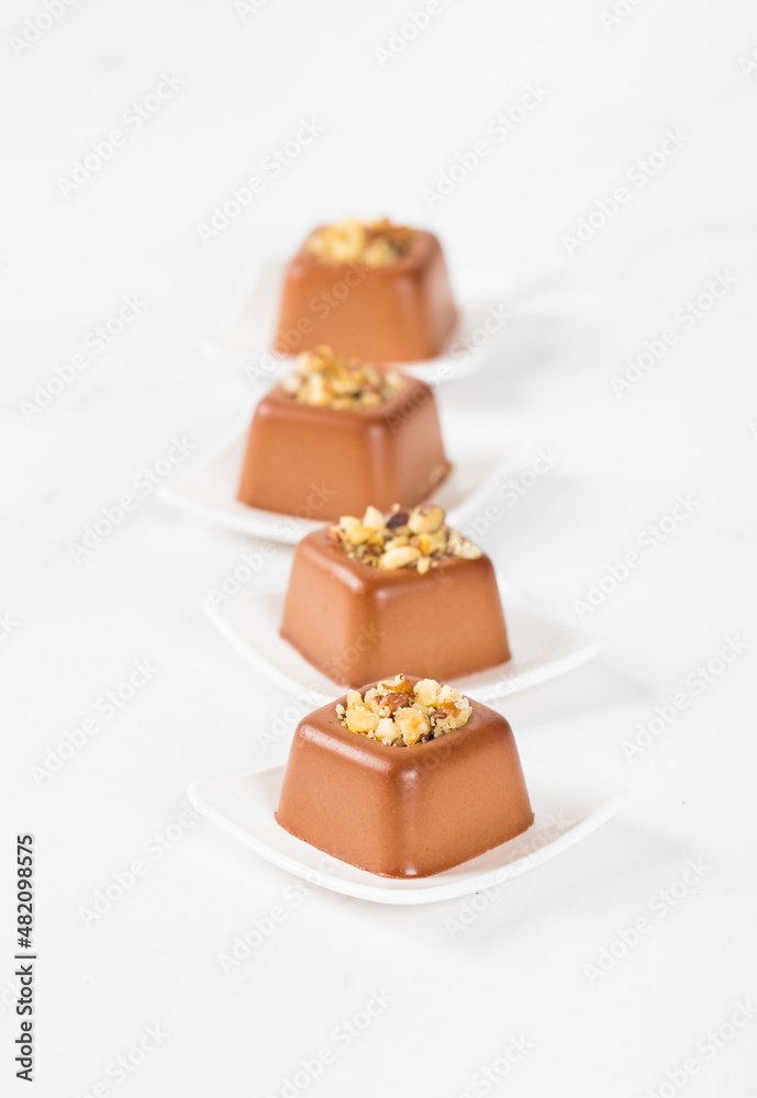Small chocolate cream pudding in the shape of a French square savarin with a filling of crushed nuts on a plate on a light background Small chocolate cream pudding in the shape of a French square savarin with a filling of crushed nuts on a plate on a light background