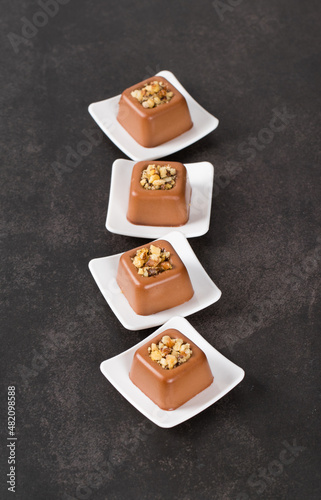 Small chocolate nut cream dessert in the shape of a square savarin on a plate on a dark gray background. Top view