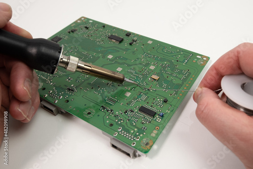 Technician repairing games console using soldering iron, soldering a capacitor.