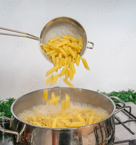 Cooking Pasta pour the penne pasta into a metal pot of boiling water. Boiled penne on a steel colander, in a cooking class. photo