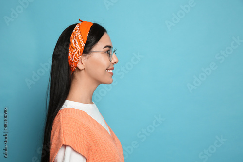 Young woman wearing stylish bandana on light blue background, space for text