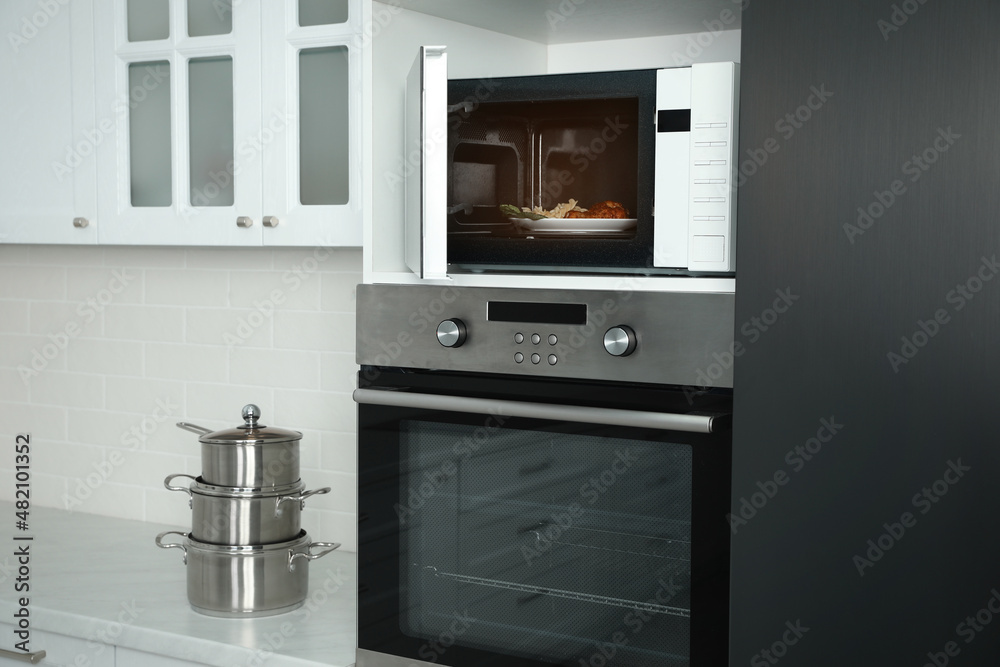 Fototapeta premium Open microwave oven with food on white shelf in kitchen
