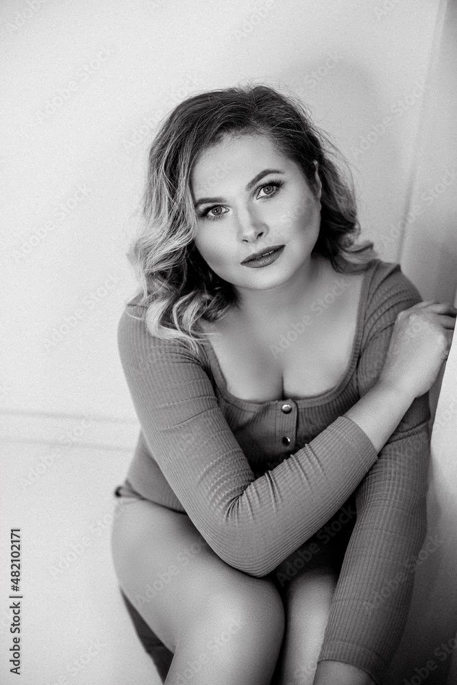 Naklejka premium Girl dressed in bodysuit. Black and white portrait of young beautiful plus size woman indoor. Body positive. Attractive plus-size woman with curvy hair. Chic of natural beauty. Film grain. Femininity