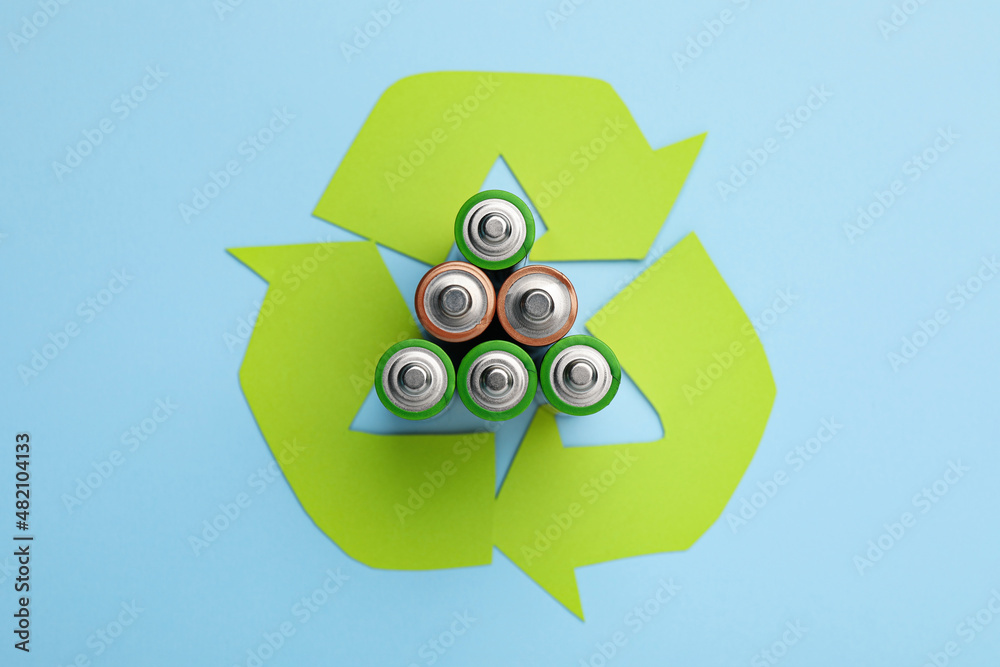 Used batteries and recycling symbol on light blue background, flat lay - obrazy, fototapety, plakaty 