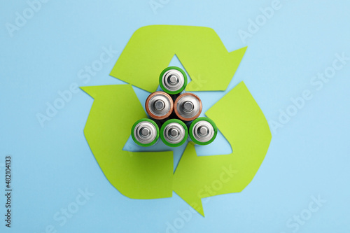 Used batteries and recycling symbol on light blue background, flat lay