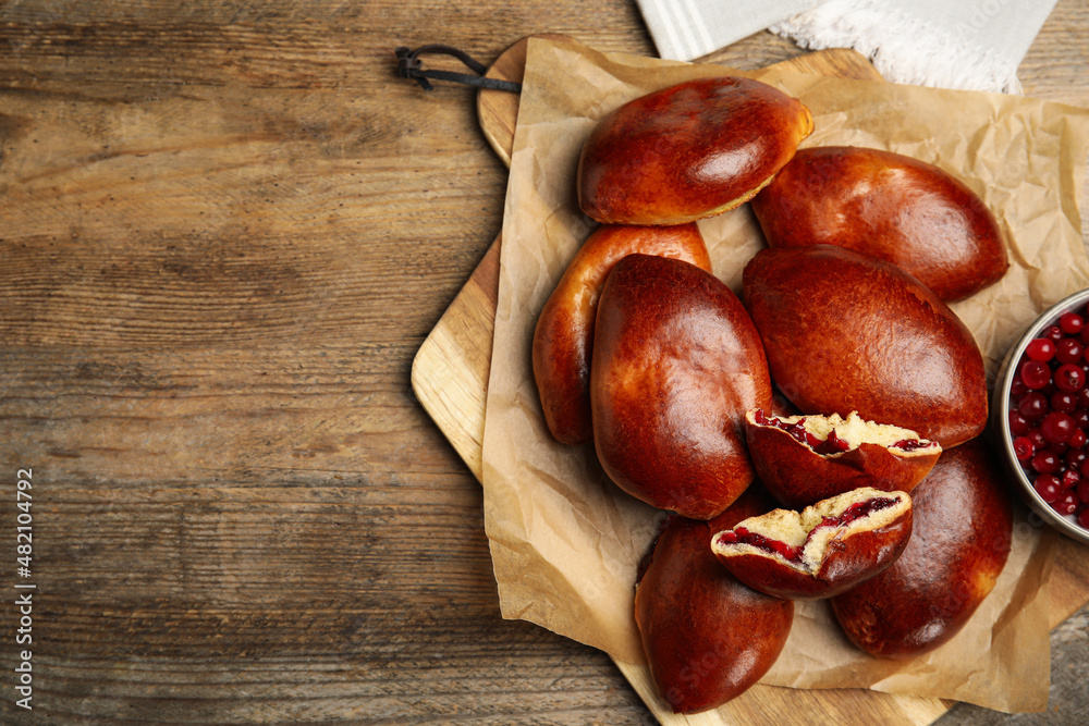 Delicious baked cranberry pirozhki on wooden table, flat lay. Space for text Delicious baked cranberry pirozhki on wooden table, flat lay. Space for text