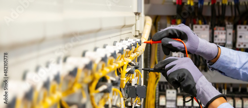 Electrical engineer using digital multi-meter measuring equipment to checking electric current voltage at circuit breaker and cable wiring system in main power distribution board.