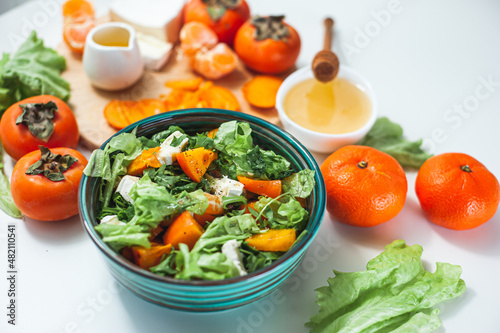 Light sweet and sour salad with persimmon, tangerines and cheese. Winter vitamin salad and ingredients on a White table. Diet food. Selective focus Vegan breakfast or lunch. Dietary vitamin nutrition